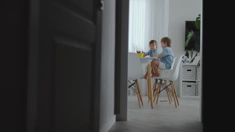 Happy-family-young-beautiful-mother-and-two-sons-draw-with-colored-pencils-sitting-at-the-table-in-the-kitchen.-The-camera-moves-in-slow-motion